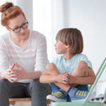 Young female school psychologist having serious conversation with smart little boy at office